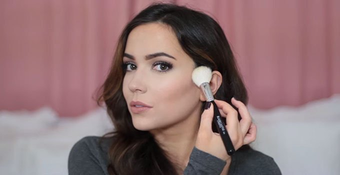 A girl apply blush on her face with brush